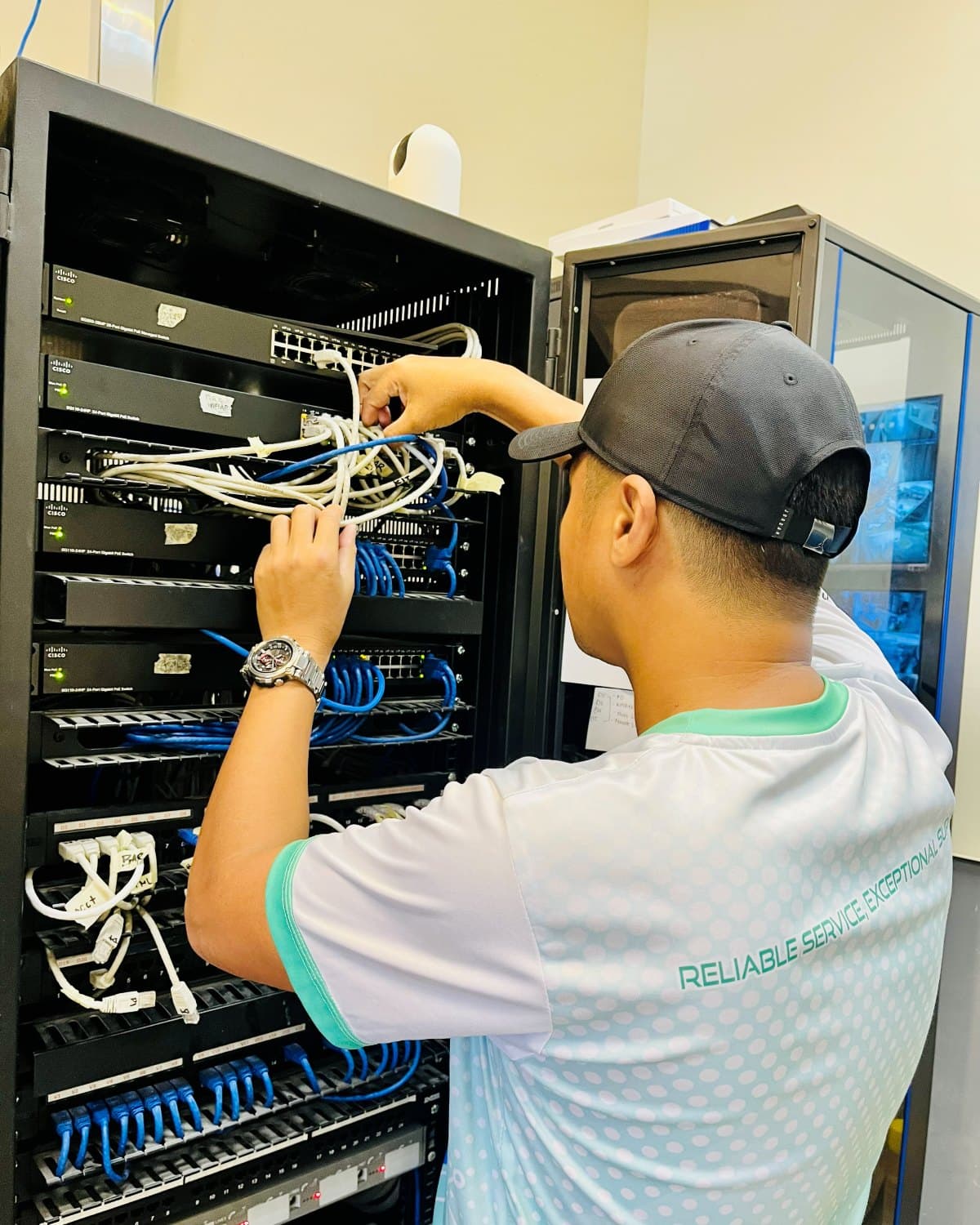 TechCare technician cabling a rack of switches and patch panels in a network room
